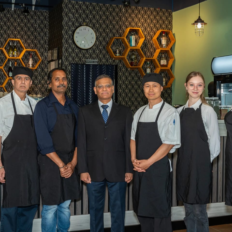 Restaurant team posing together in aprons beneath honeycomb shelves and pendant lights.