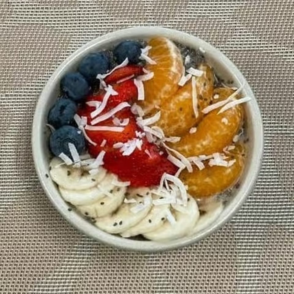 Acai bowl topped with blueberries, strawberries, banana slices, orange segments, and shredded coconut.